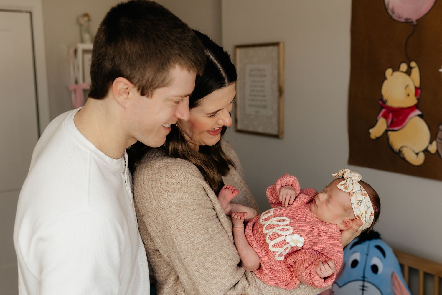 New parents smile adoringly at their newborn baby girl in a decorated nursery.