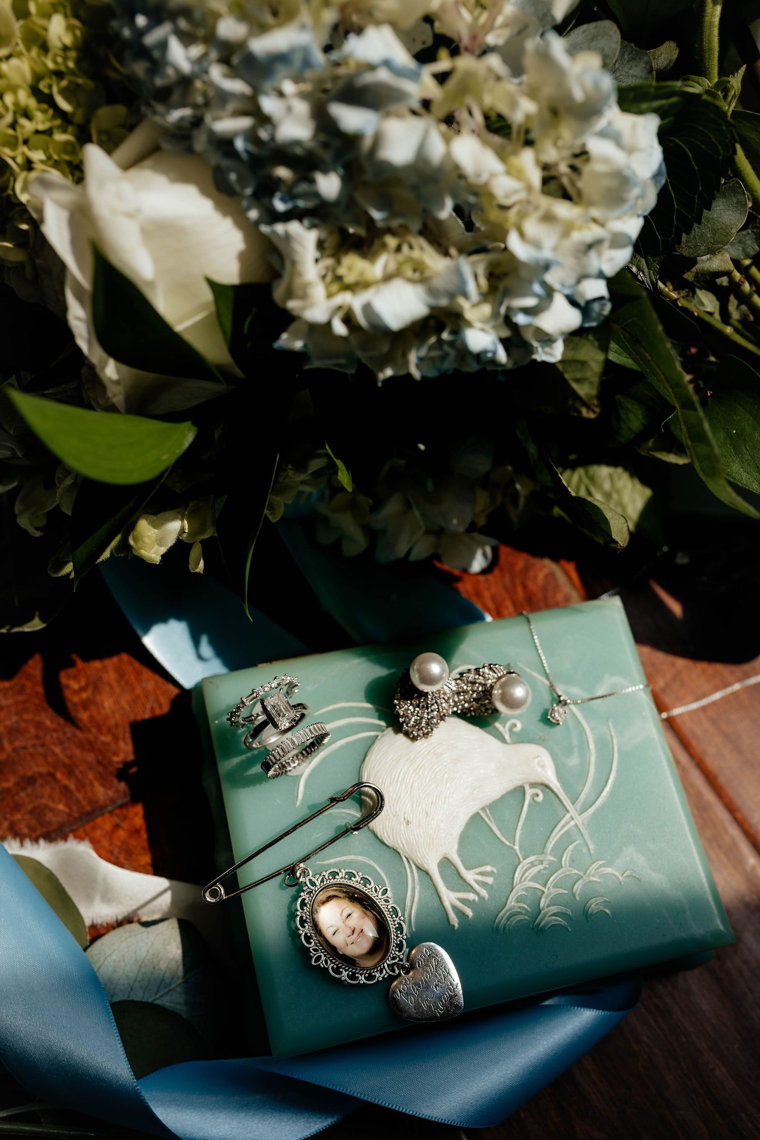 Teal wedding journal adorned with vintage brooches and pins beside a white hydrangea bridal bouquet.
