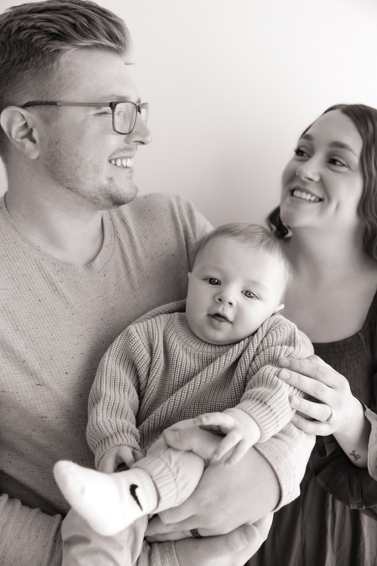 Black and white photo of smiling parents holding their baby together.