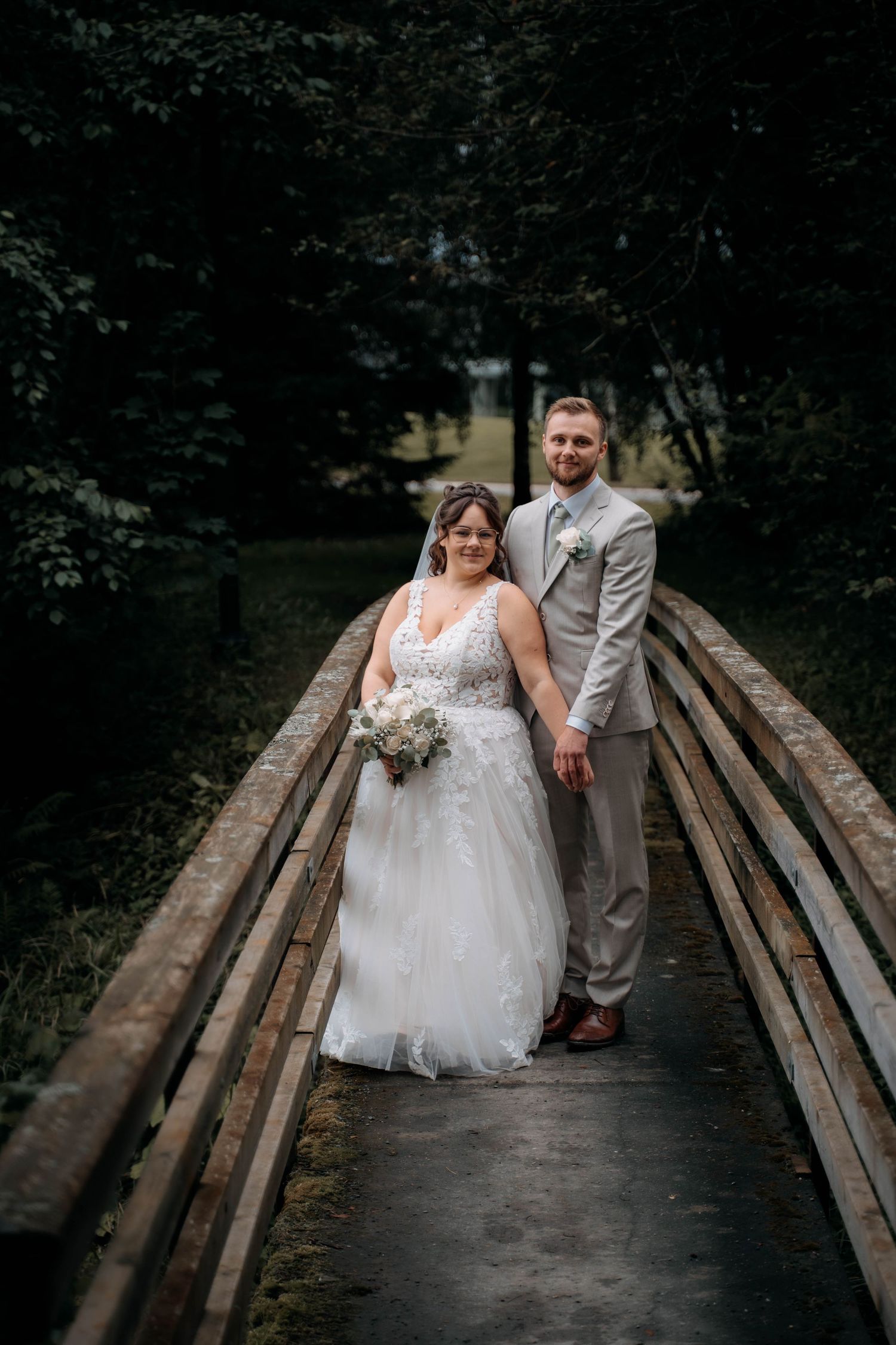 Bride and groom holding hands on a wooden bridge surrounded by lush greenery on their wedding day.