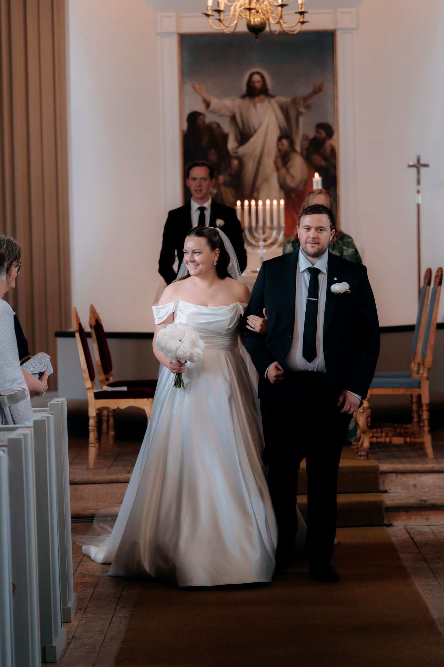 Bride and groom walking down church aisle during wedding ceremony with Jesus painting and candles in background.