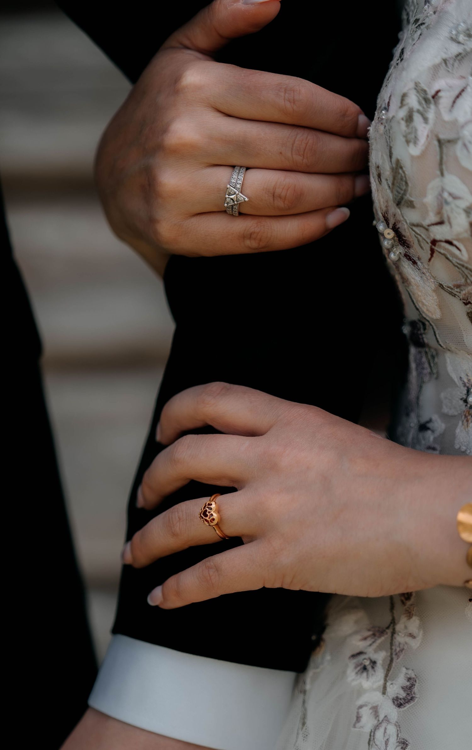 Close-up of two hands adorned with elegant rings, one silver diamond band and one gold ornate ring, embracing tenderly.
