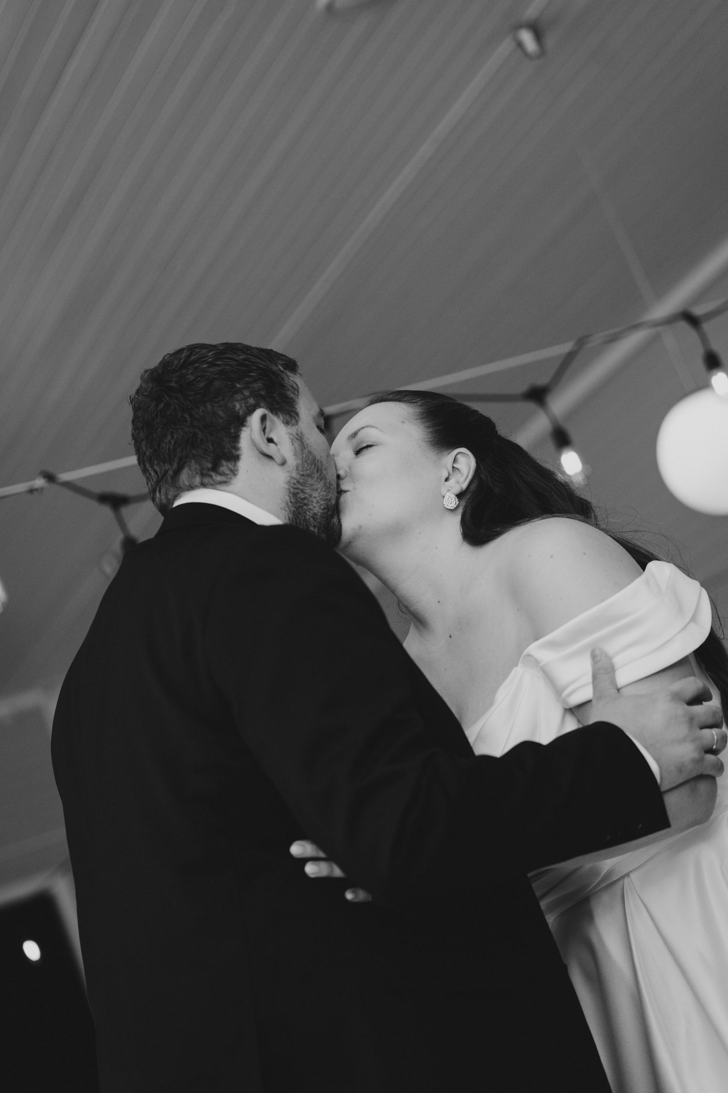 Black and white photo of a bride and groom sharing a kiss during their first dance at a wedding reception.