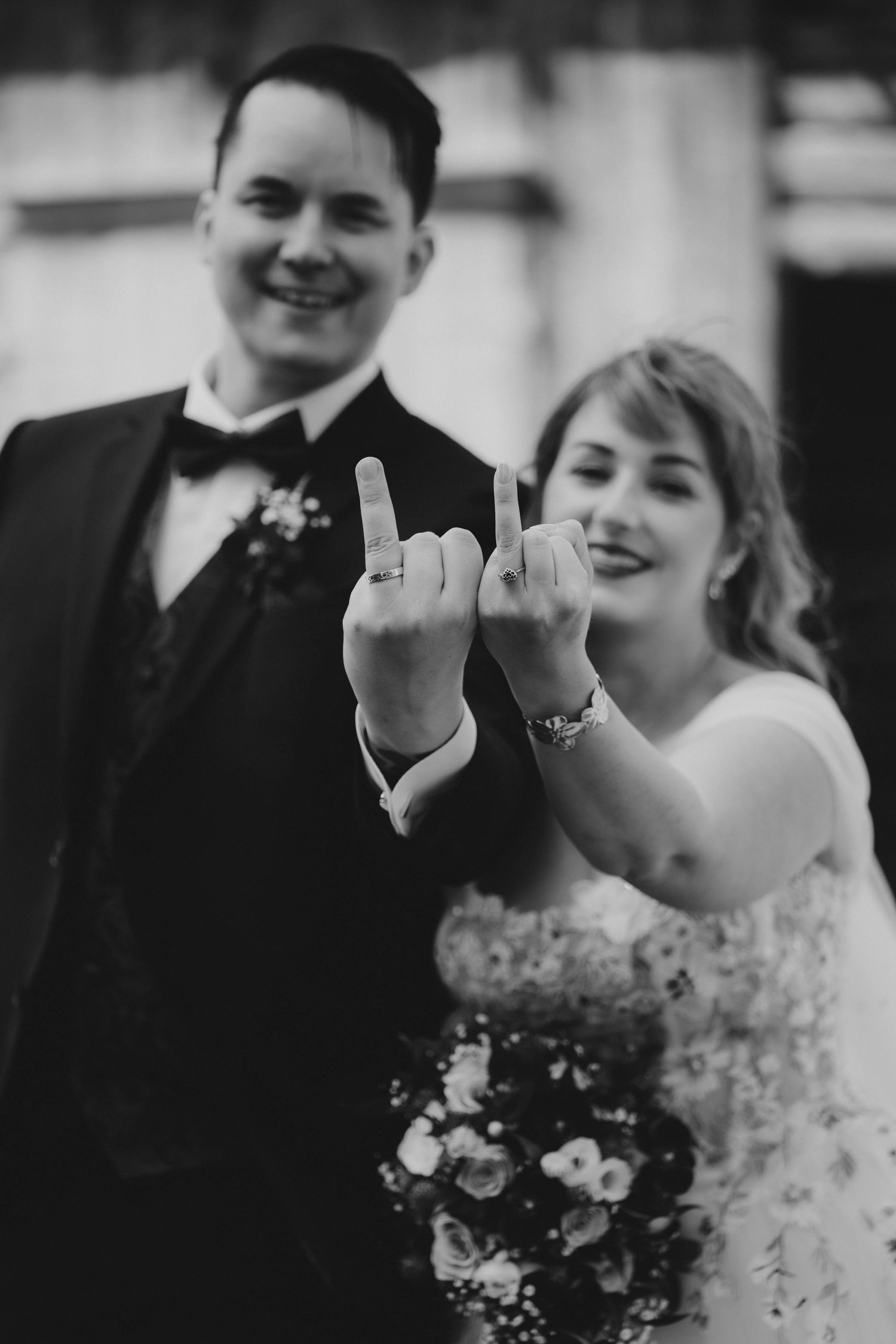 Black and white wedding photo of smiling bride and groom showing off their wedding rings on their fingers.