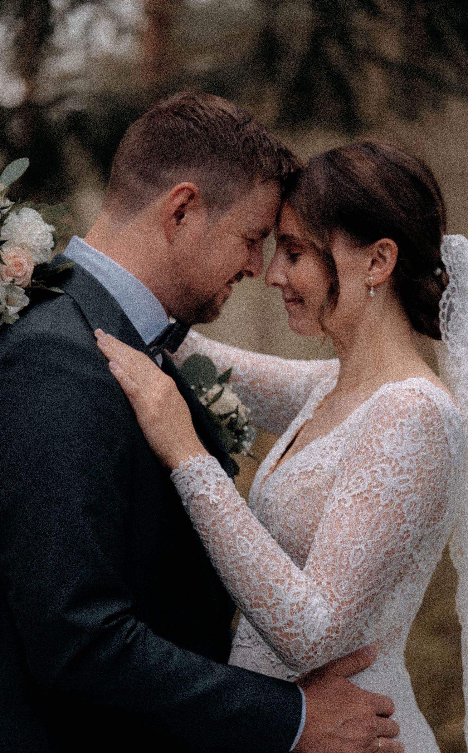 Bride and groom share an intimate forehead touch moment, bride wearing long-sleeve lace wedding dress outdoors.