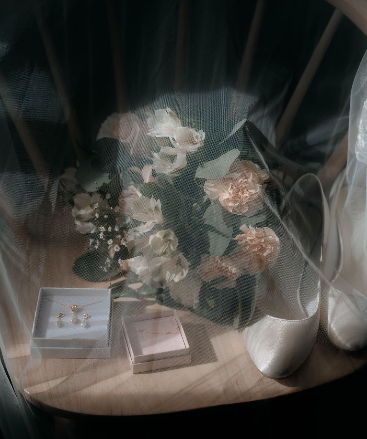 Elegant bridal flat lay with white floral bouquet, pearl earrings in box, and satin heels on wooden surface.