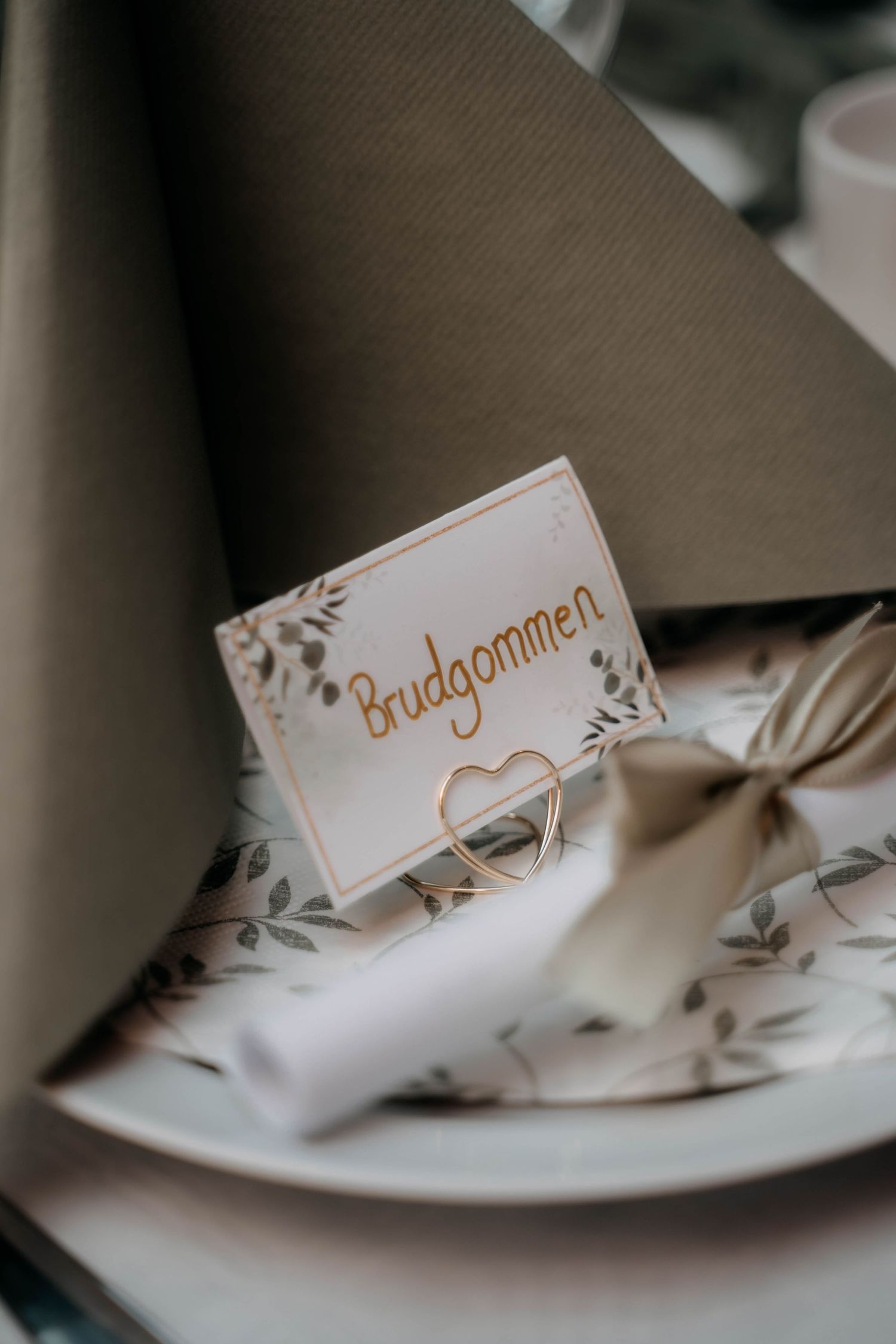 Elegant wedding place card reading Brudgommen in gold script on a decorated table setting.