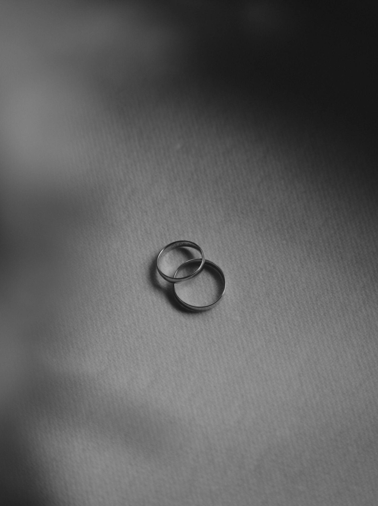 Two silver wedding bands resting together on a soft gray surface in a black and white photo.