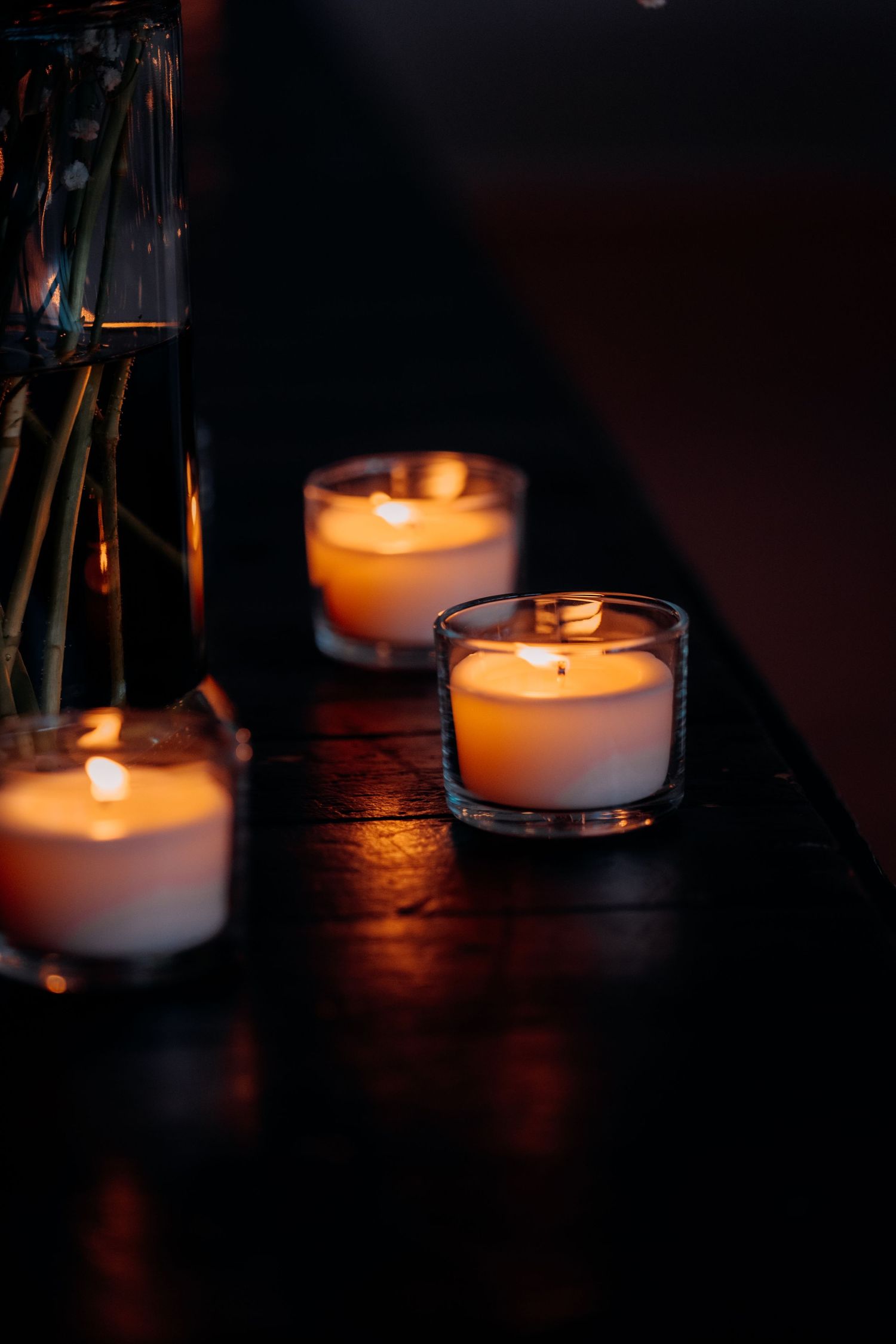 Three glowing tea light candles in glass holders arranged on a dark wooden surface for a romantic ambiance.