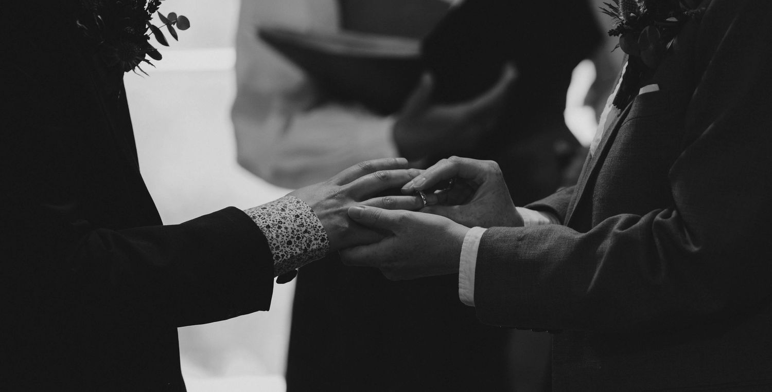 Black and white photo of couple exchanging wedding rings during ceremony.