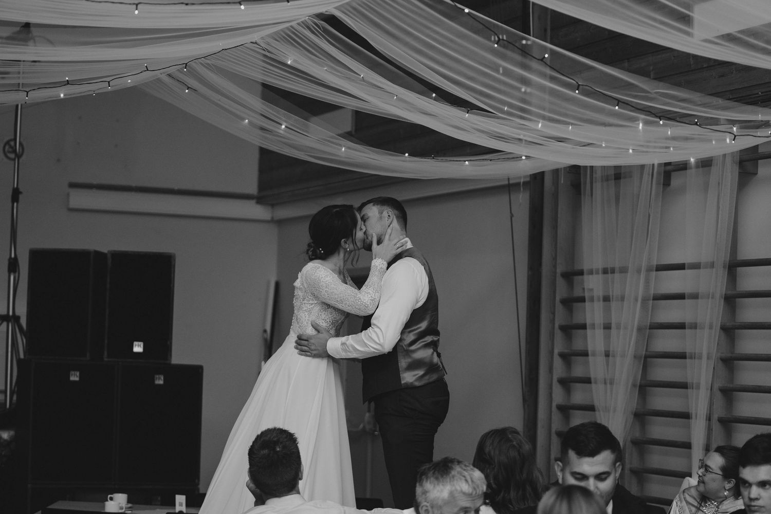 Black and white photo of a bride and groom sharing their first kiss at their wedding reception.