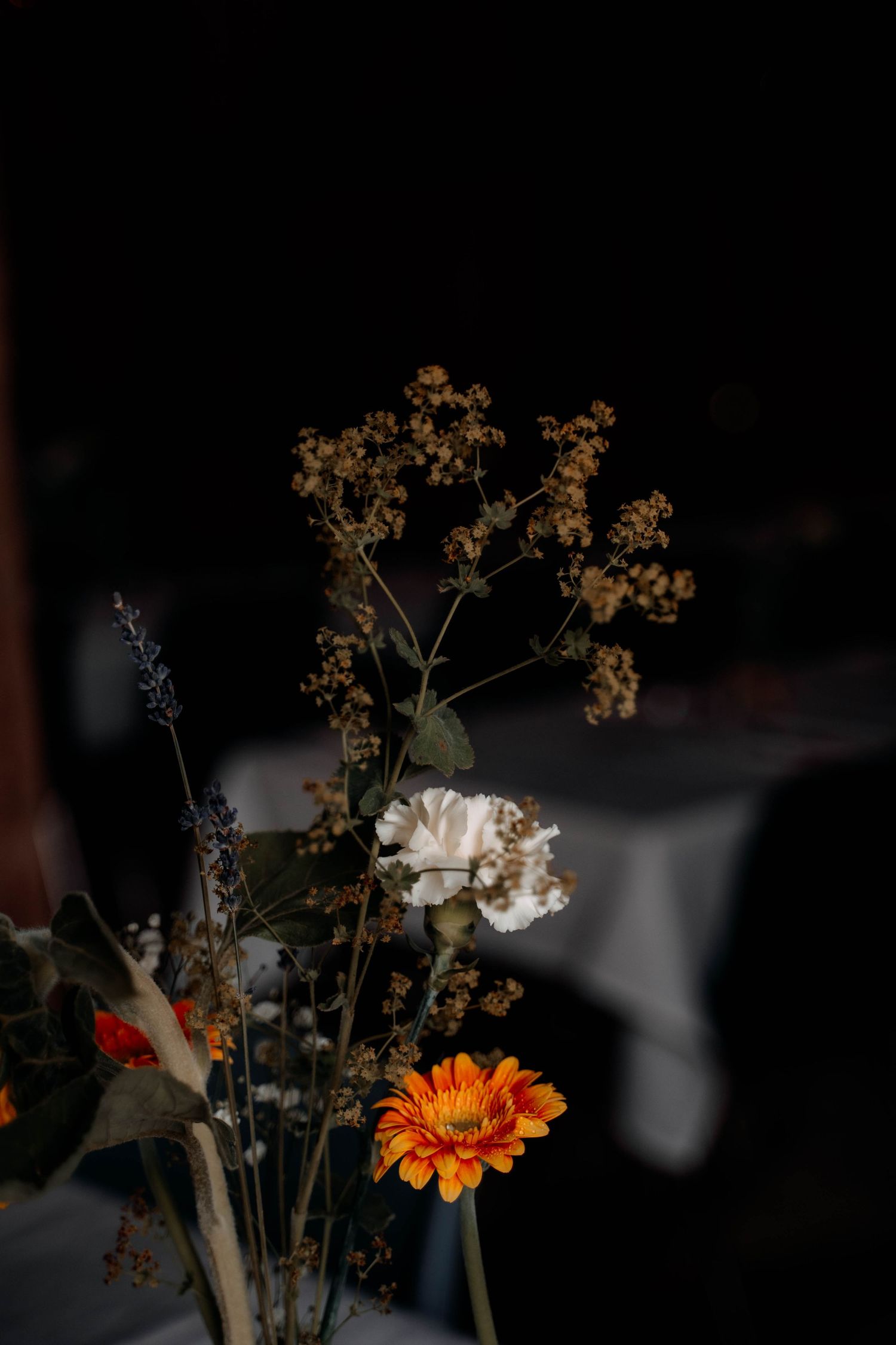 Autumn floral arrangement with orange gerbera, white carnation, and dried wildflowers against dark background.