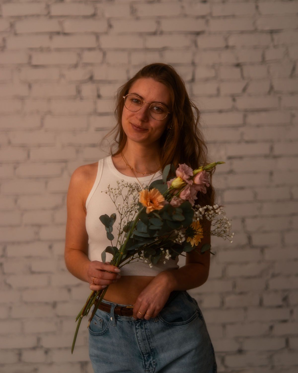 Frau mit Blumen in der Hand steht vor Backsteinwand