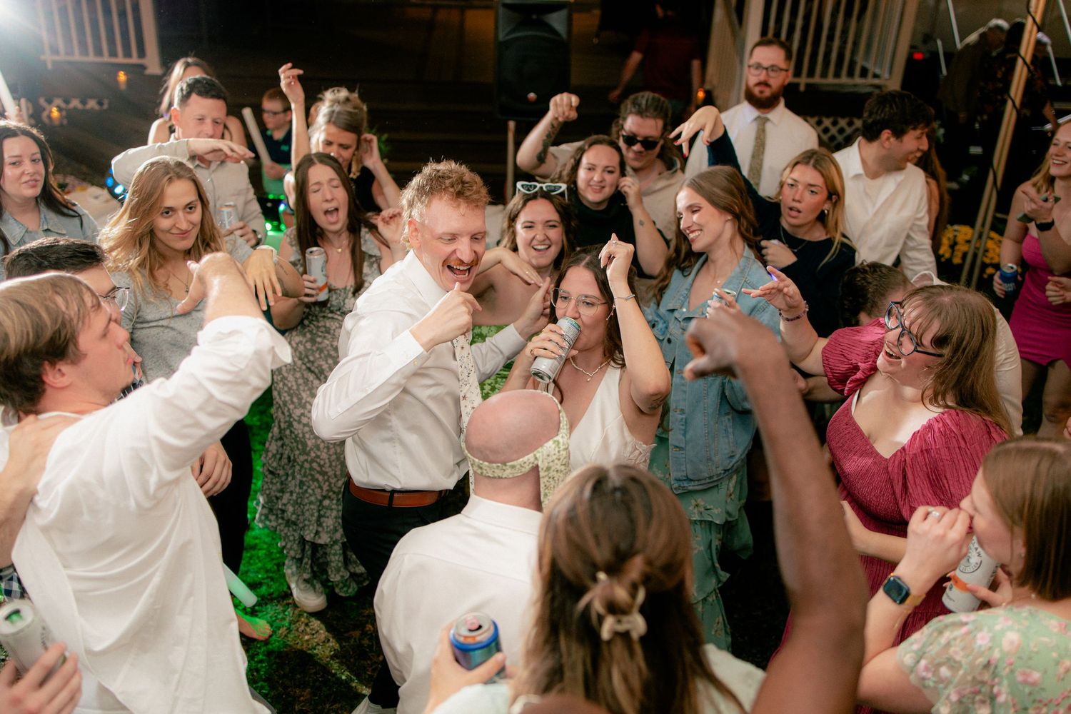 Joyful bride and groom celebrate with energetic wedding guests on the dance floor at reception.