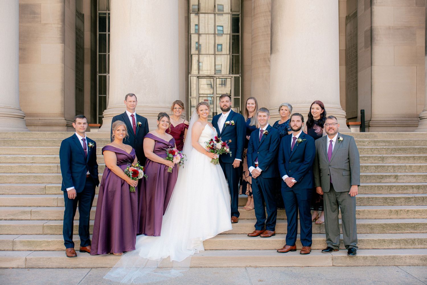 Wedding party posing on stone steps, bridesmaids in purple dresses and groomsmen in navy suits.