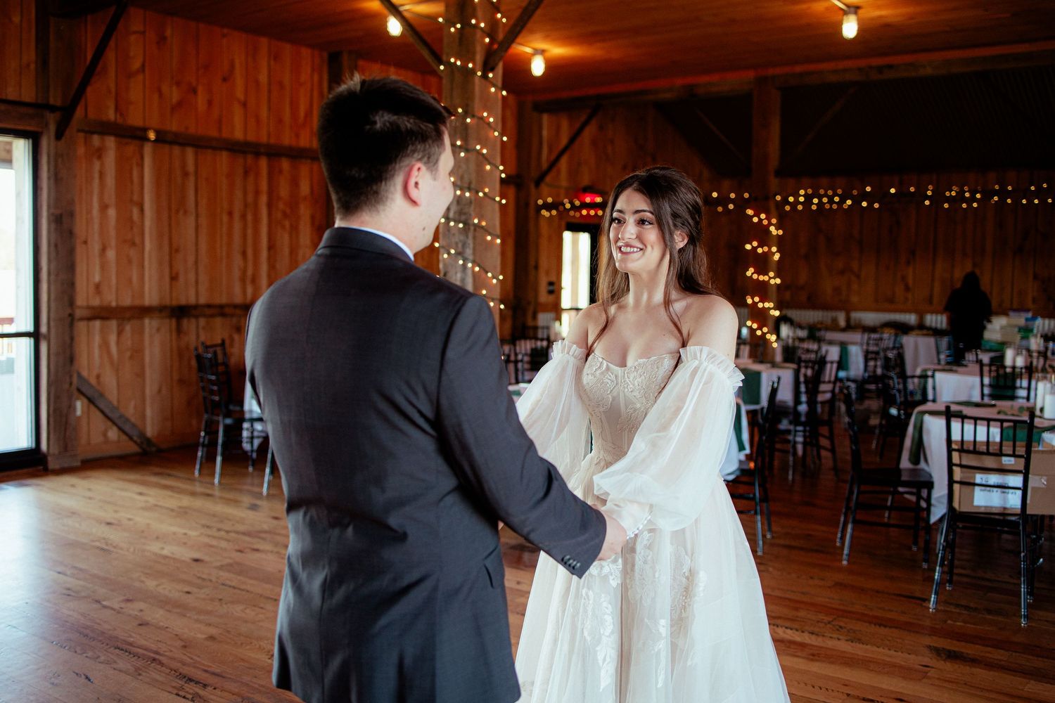 Bride and groom share first dance in a rustic barn venue adorned with warm string lights.