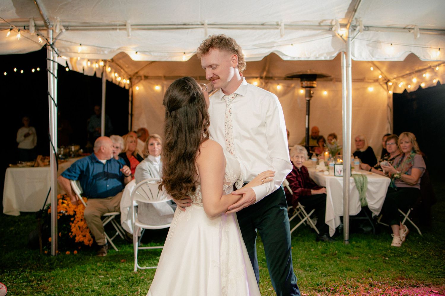 Bride and groom share romantic first dance under string lights in an elegant outdoor tent reception.