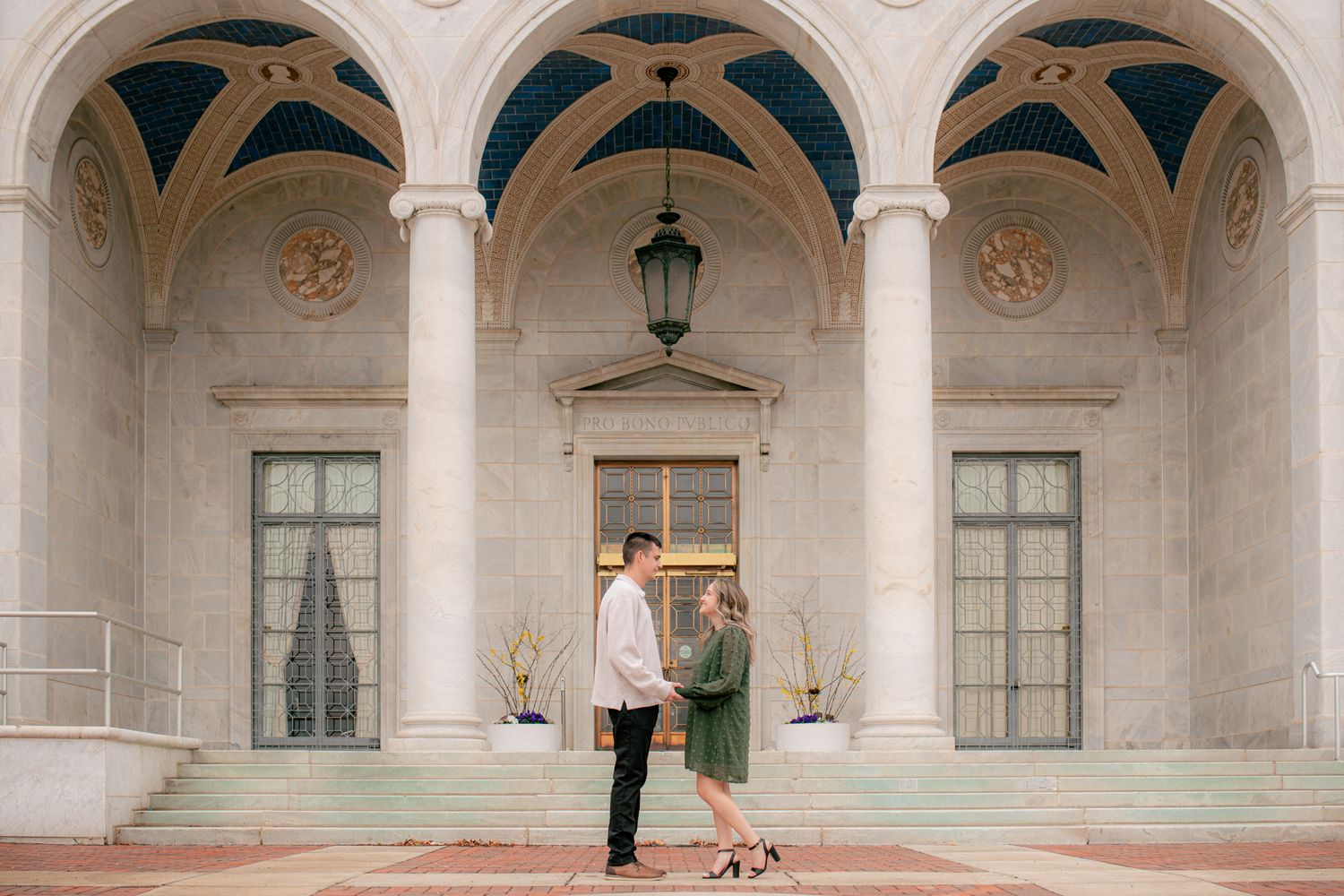 Couple holding hands facing each other under grand arched colonnade of a classical building.