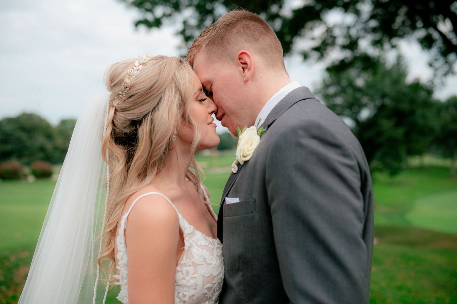 Bride and groom sharing an intimate forehead touch moment on a lush green golf course.