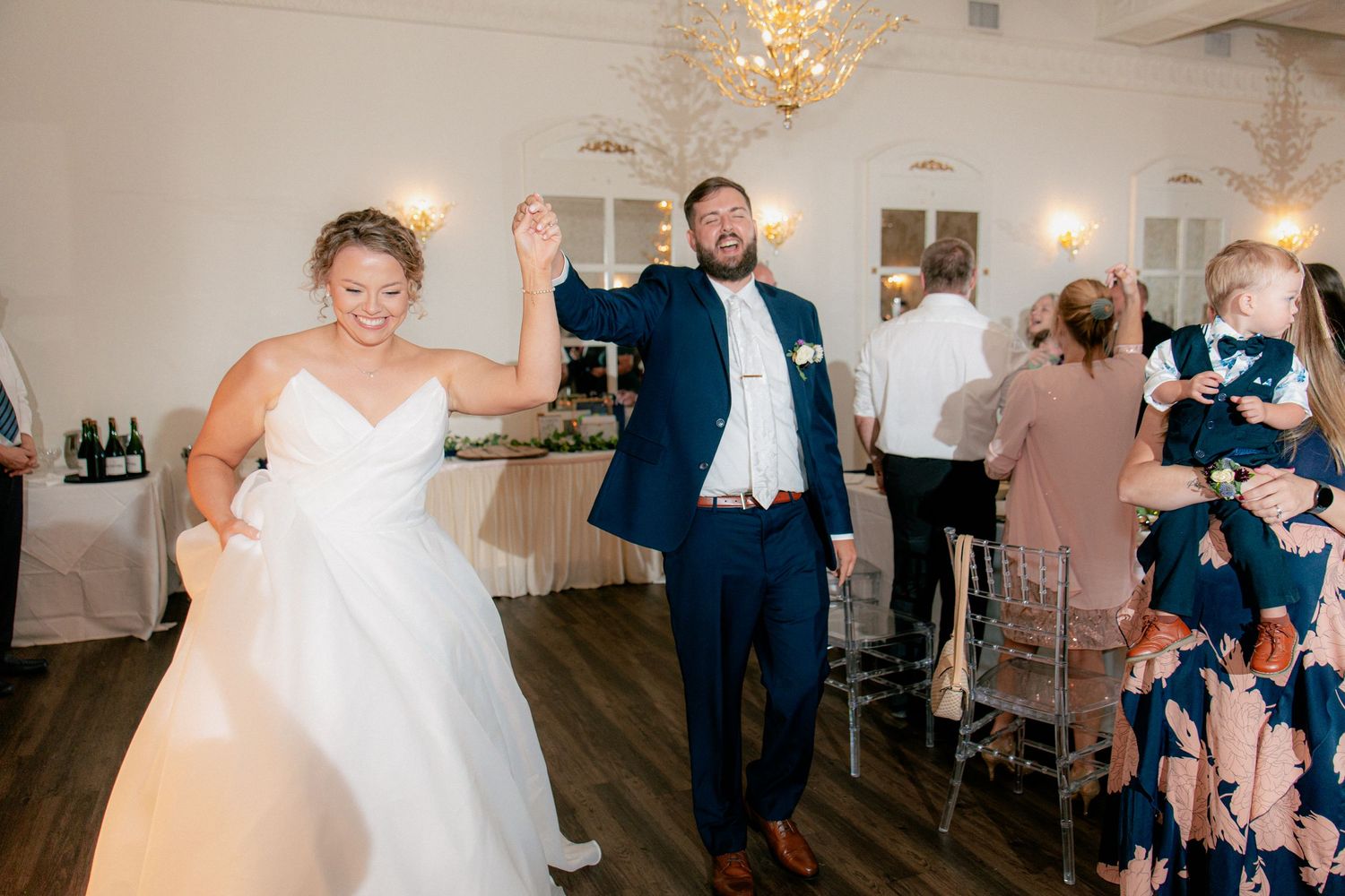 Smiling bride and groom make a grand entrance onto the wedding reception dance floor.