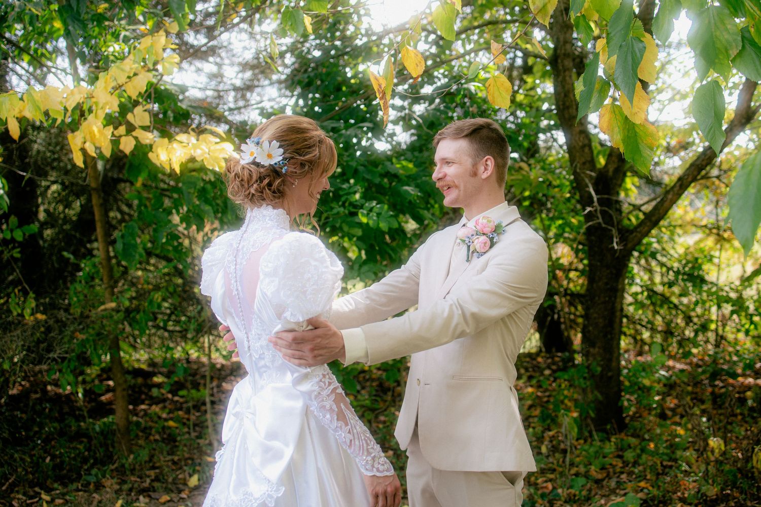 Bride and groom share a tender moment holding hands outdoors surrounded by lush green and yellow autumn foliage.