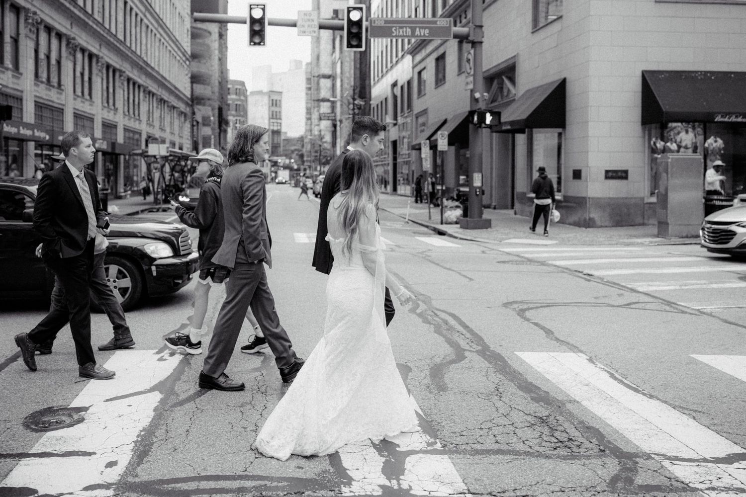 Black and white photo of bride and groom crossing busy city street intersection on wedding day.