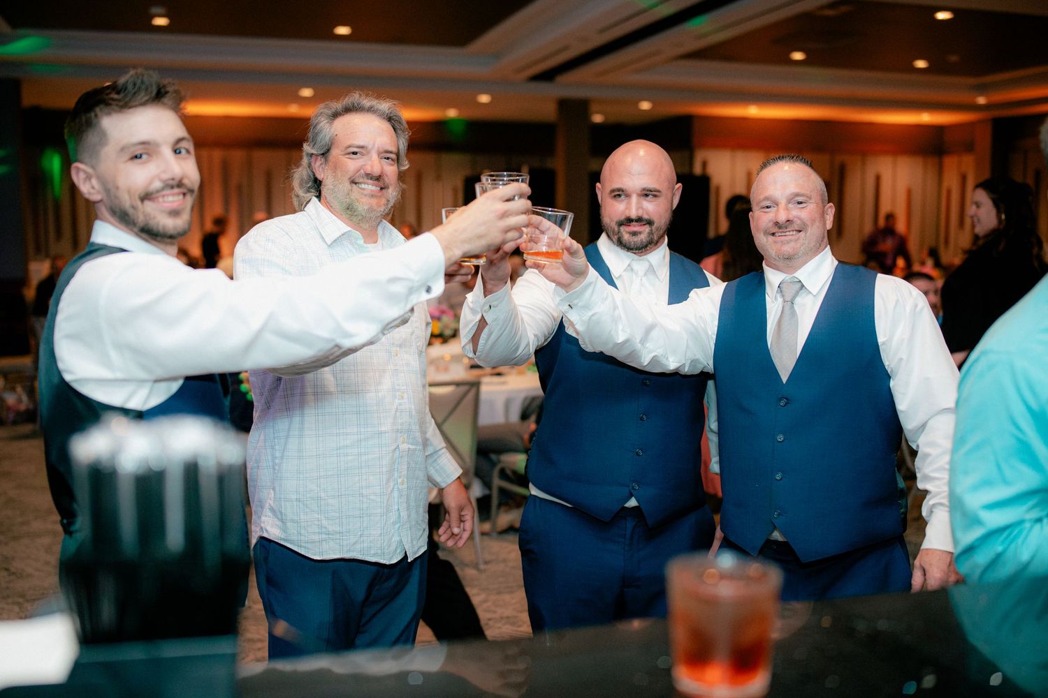 Four men in formal attire raising cocktail glasses in a celebratory toast at wedding reception.
