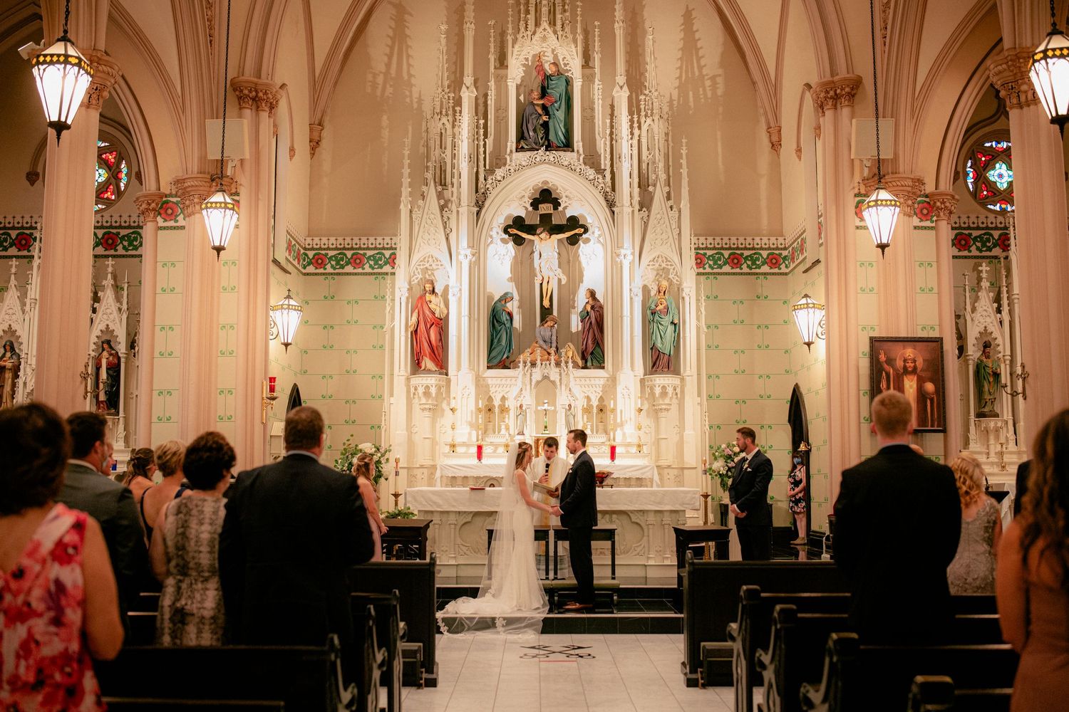 Wide-angle view of elegant church wedding ceremony with couple at ornate altar and seated guests.