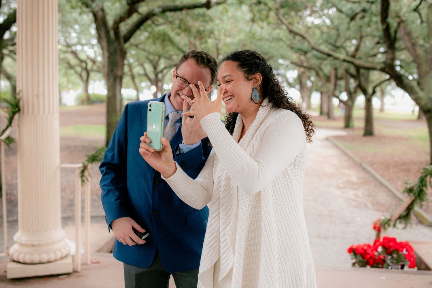 Newlywed couple laughs joyfully while sharing a phone moment together after outdoor wedding ceremony.