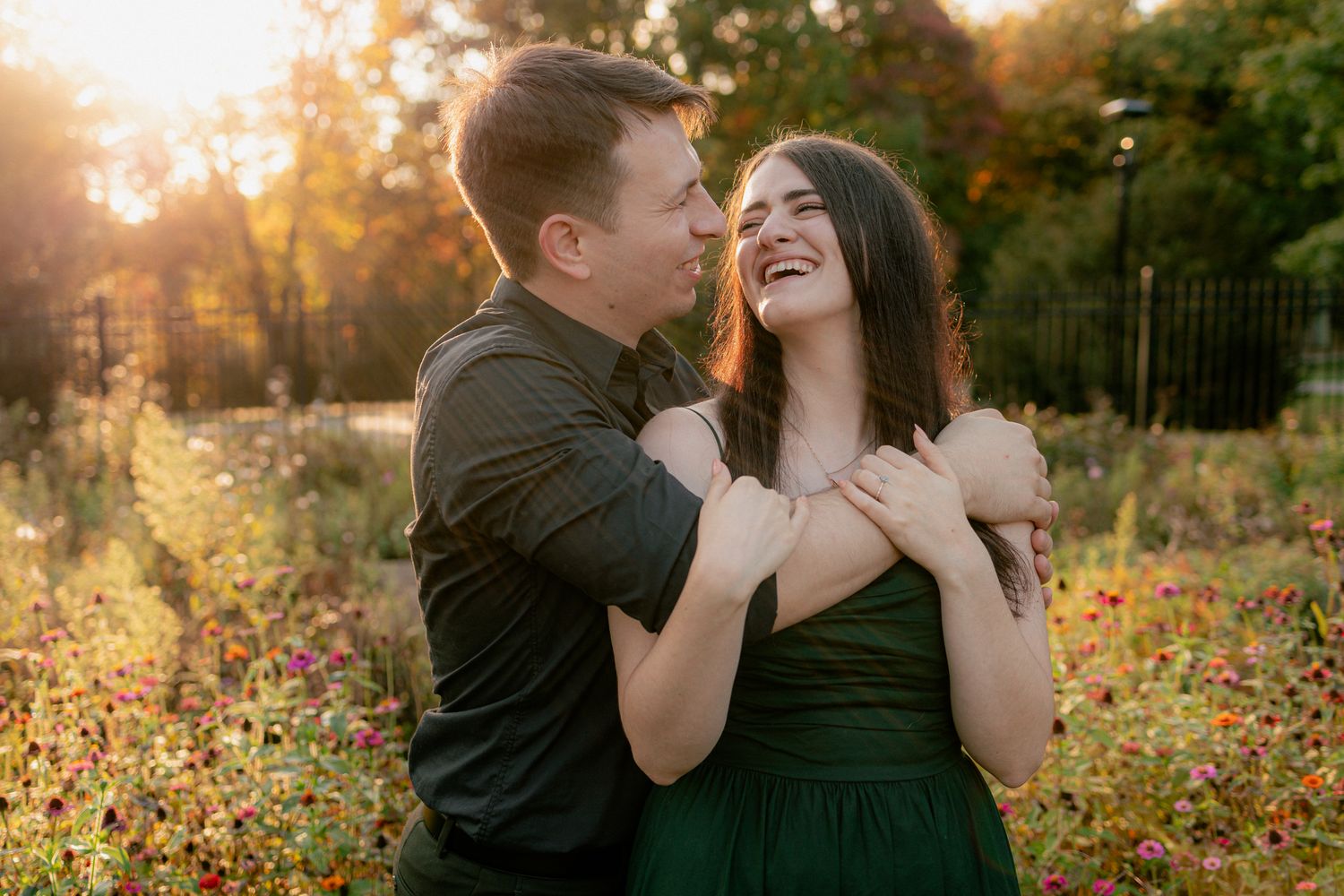Laughing couple embracing at golden hour in a colorful autumn flower garden with warm backlight.