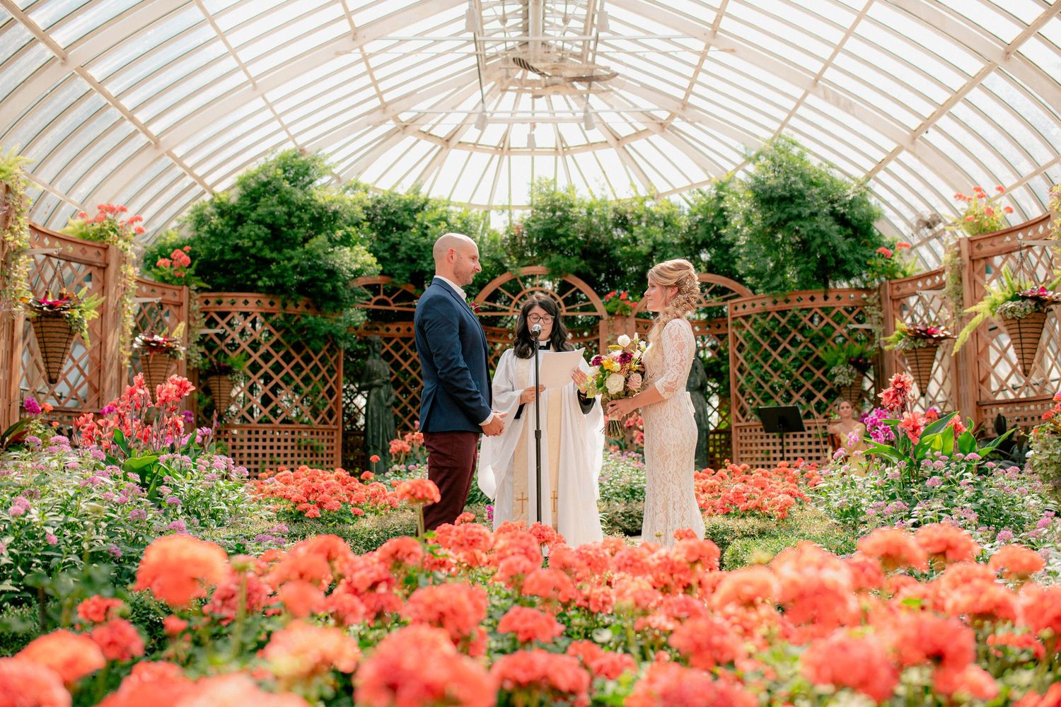Intimate greenhouse wedding ceremony with couple exchanging vows surrounded by vibrant orange flowers.
