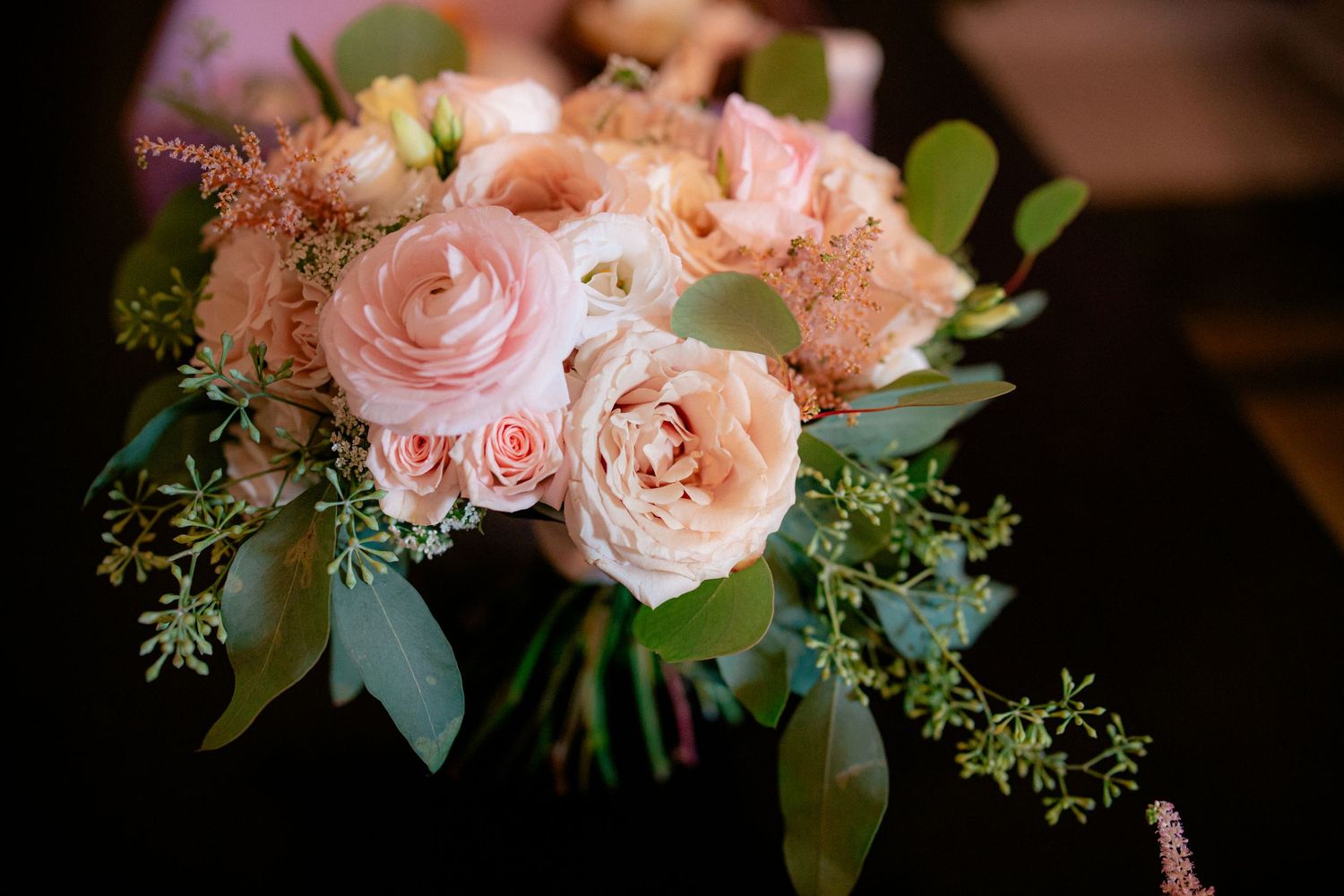 Close-up of a romantic bridal bouquet featuring blush roses, ranunculus, and eucalyptus greenery.