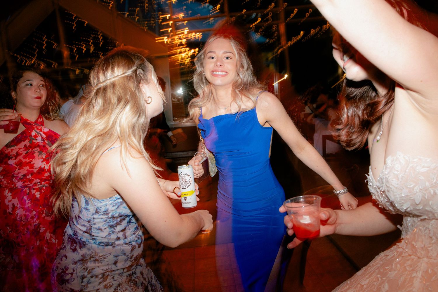 Guests in colorful dresses dancing and holding drinks on the wedding reception dance floor.