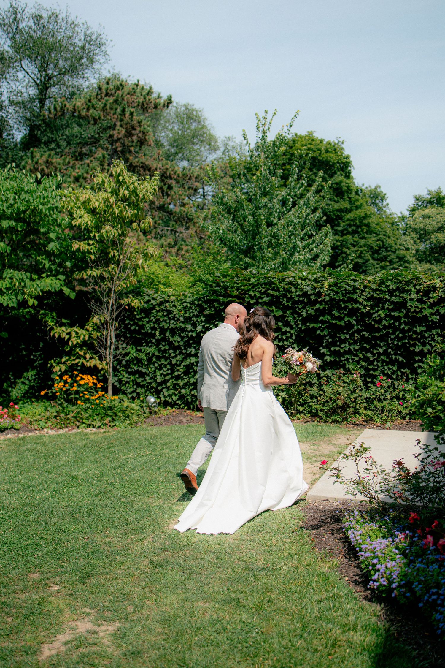 Bride and groom sharing a kiss in a lush garden, bride holding a bouquet in a flowing white gown.