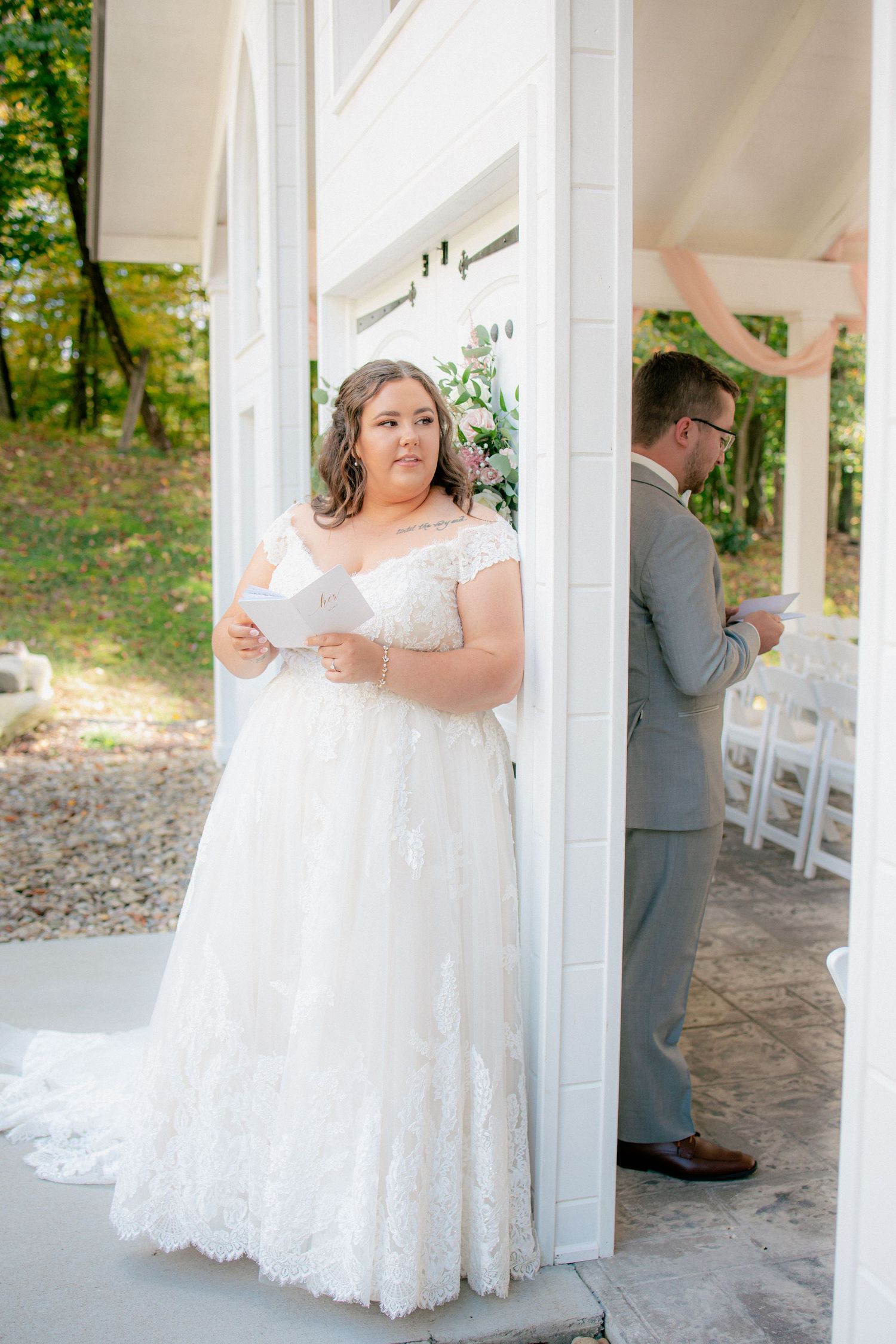 Bride reads vows during outdoor first look with groom at elegant white pavilion wedding venue.