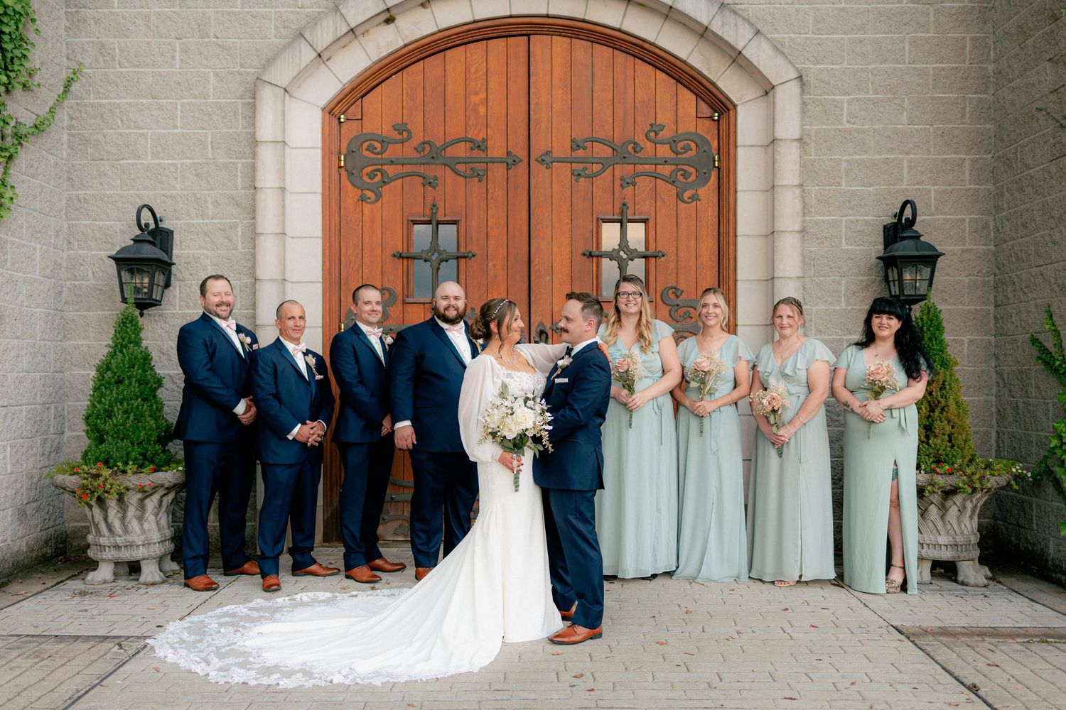 Wedding party posing in front of stone church doors, bridesmaids in mint green and groomsmen in navy.