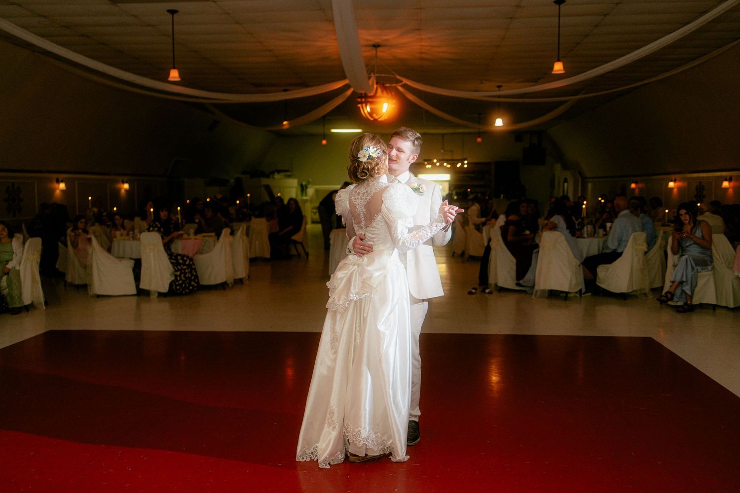 Bride and groom share an intimate first dance on a red carpet in a decorated wedding reception hall.
