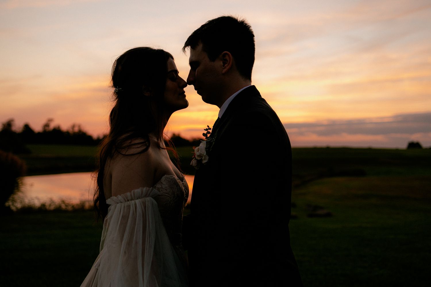Romantic silhouette of bride and groom facing each other against a vibrant orange and purple sunset sky.