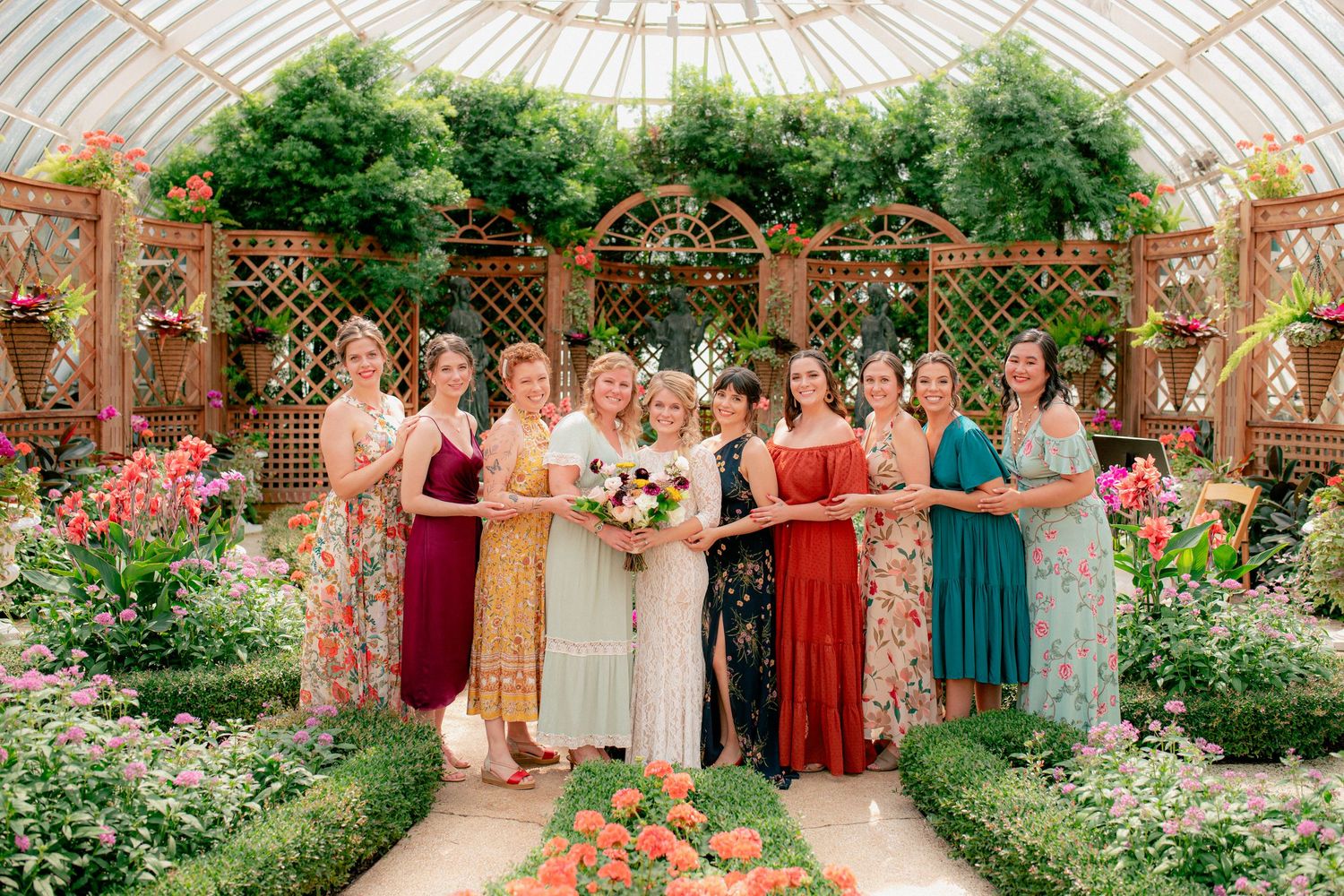 Bride and bridesmaids in colorful dresses pose together inside a floral greenhouse.