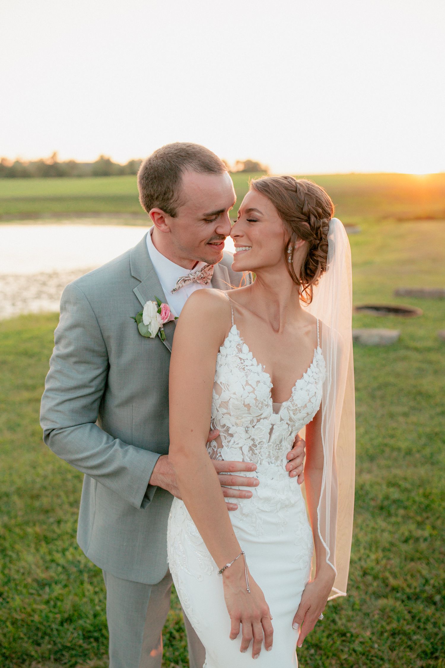 Bride and groom sharing a romantic sunset moment outdoors, bride in lace gown with veil, groom in gray suit.