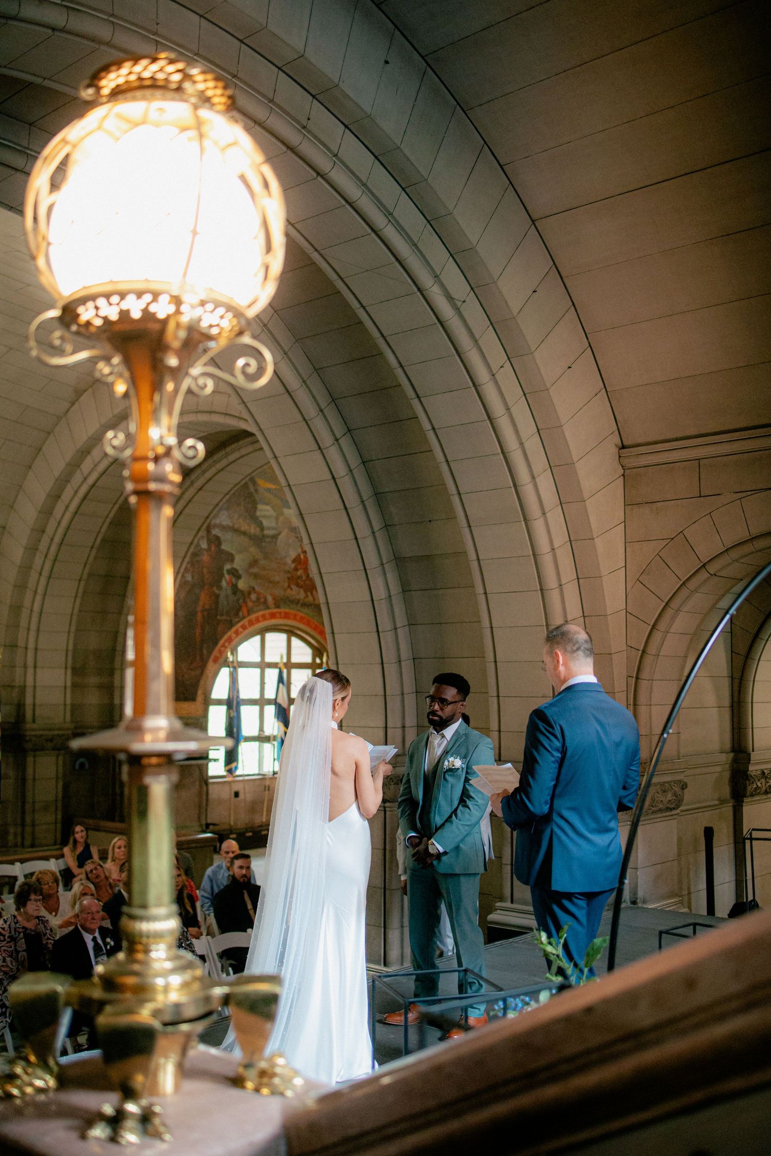 Bride and groom exchange vows at elegant stone courthouse with ornate brass lamp.