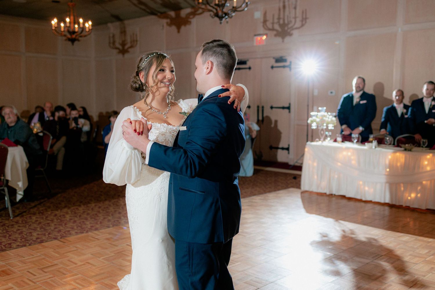 Bride and groom share romantic first dance in warmly lit ballroom wedding reception.