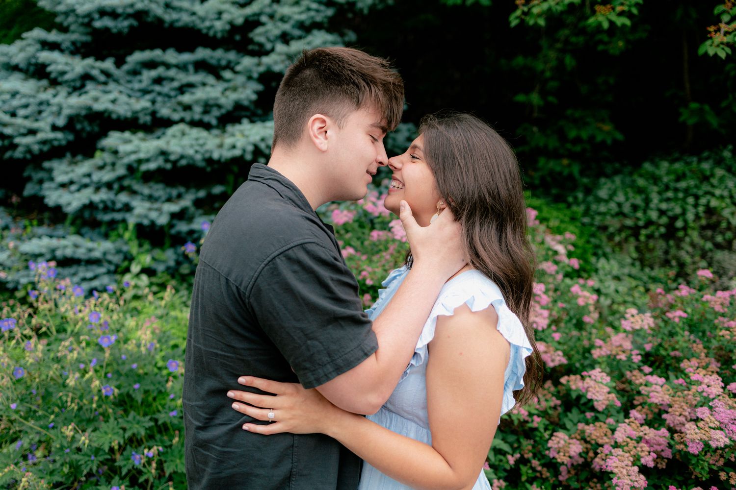 Young couple almost kissing in a colorful garden, man gently holding womans face in his hands.