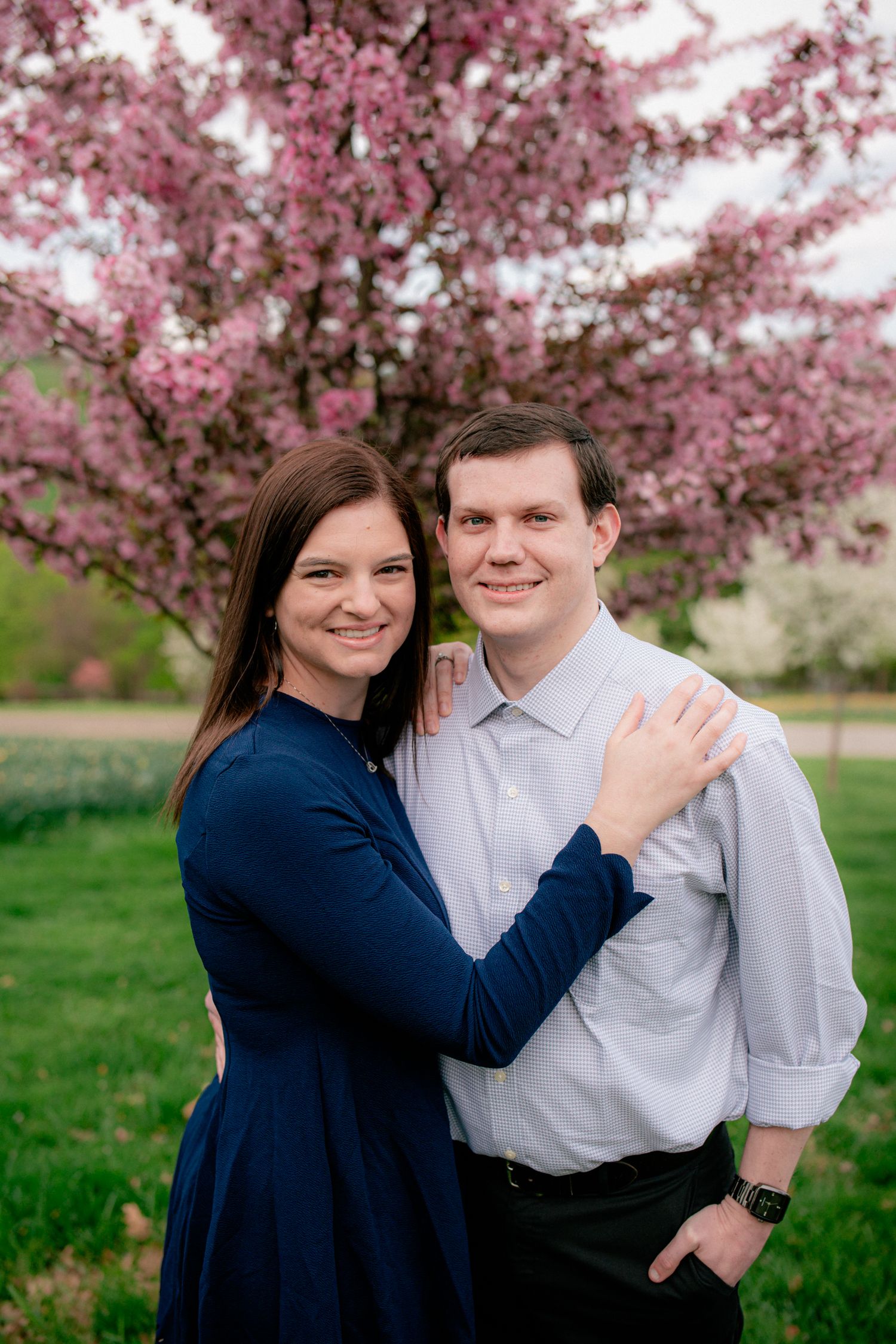 Smiling couple embracing in front of blooming pink cherry blossom tree in spring park.