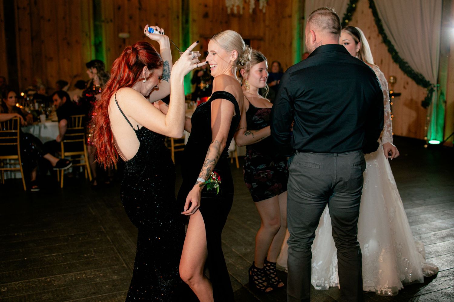 Wedding guests dancing and taking selfies in elegant black dresses at barn reception.