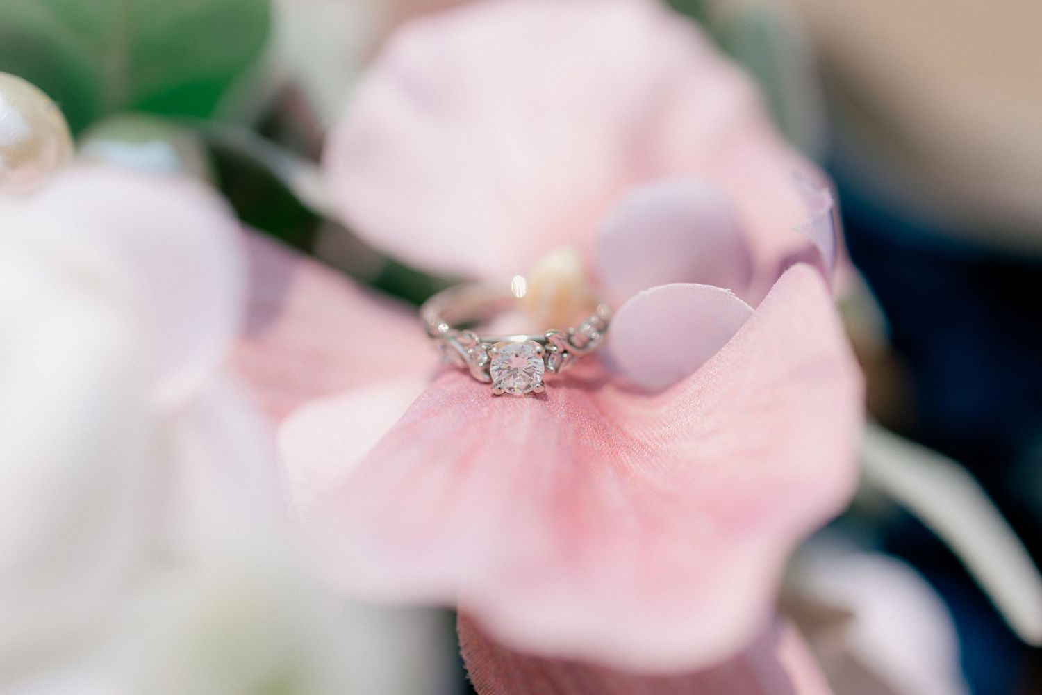 Close-up of a sparkling diamond engagement ring resting on soft pink flower petals.