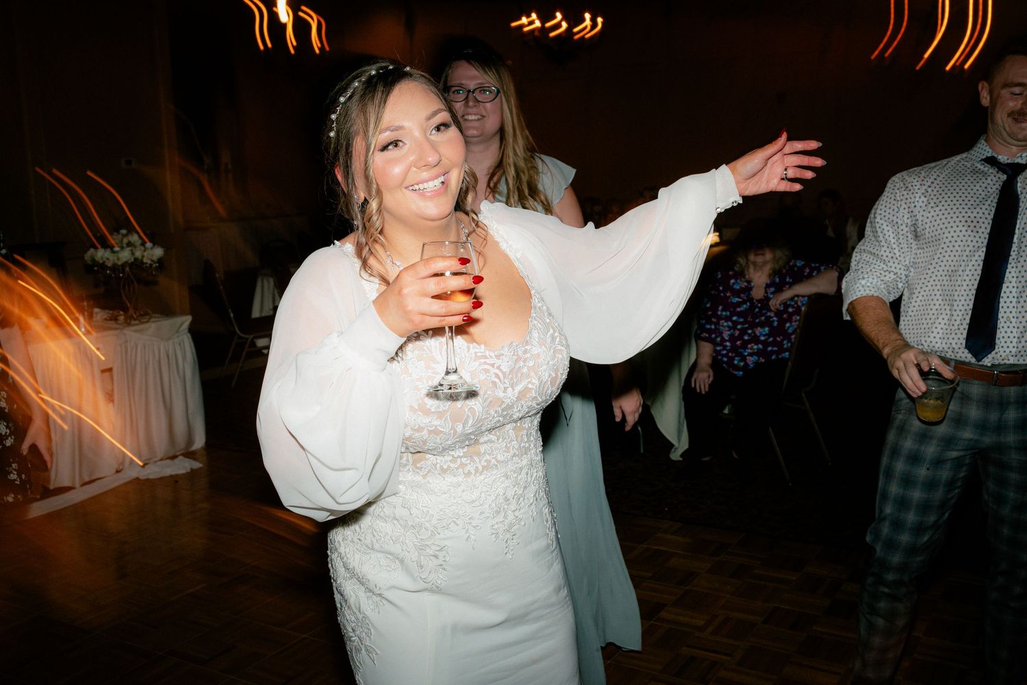 Bride in white gown dancing joyfully at wedding reception holding a cocktail glass.