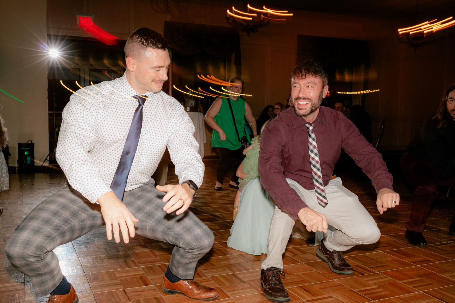 Two male wedding guests doing fun squatting dance moves on reception dance floor.