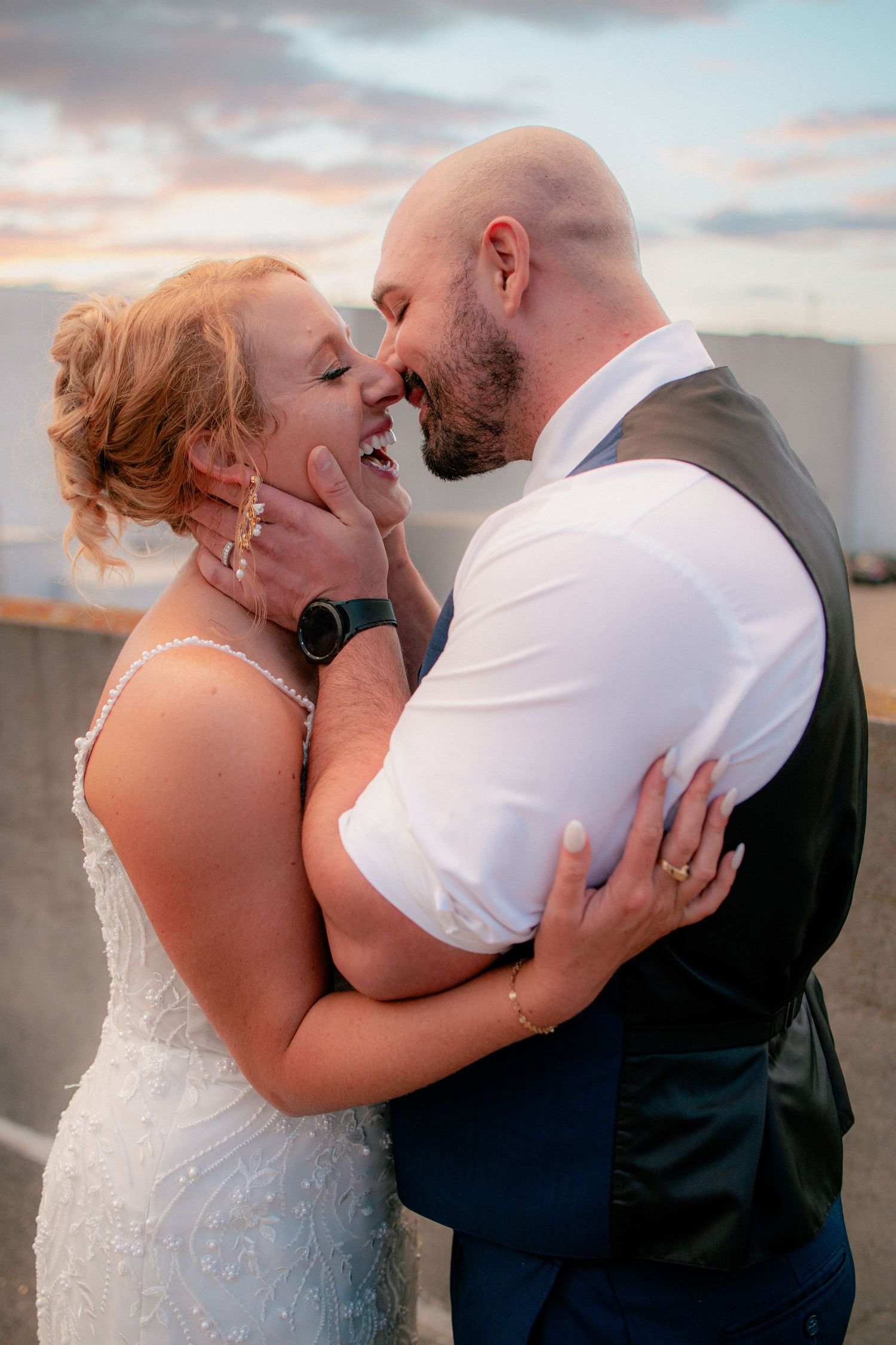 Joyful bride and groom share a tender nose-to-nose moment at sunset on a rooftop wedding venue.