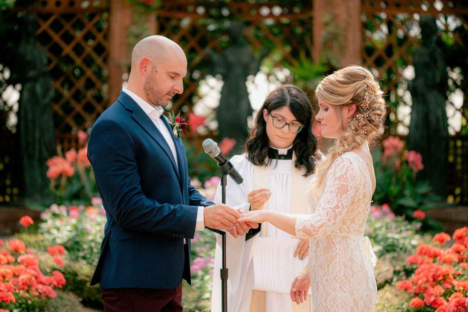 Groom places wedding ring on bride's finger during emotional greenhouse ceremony with officiant.